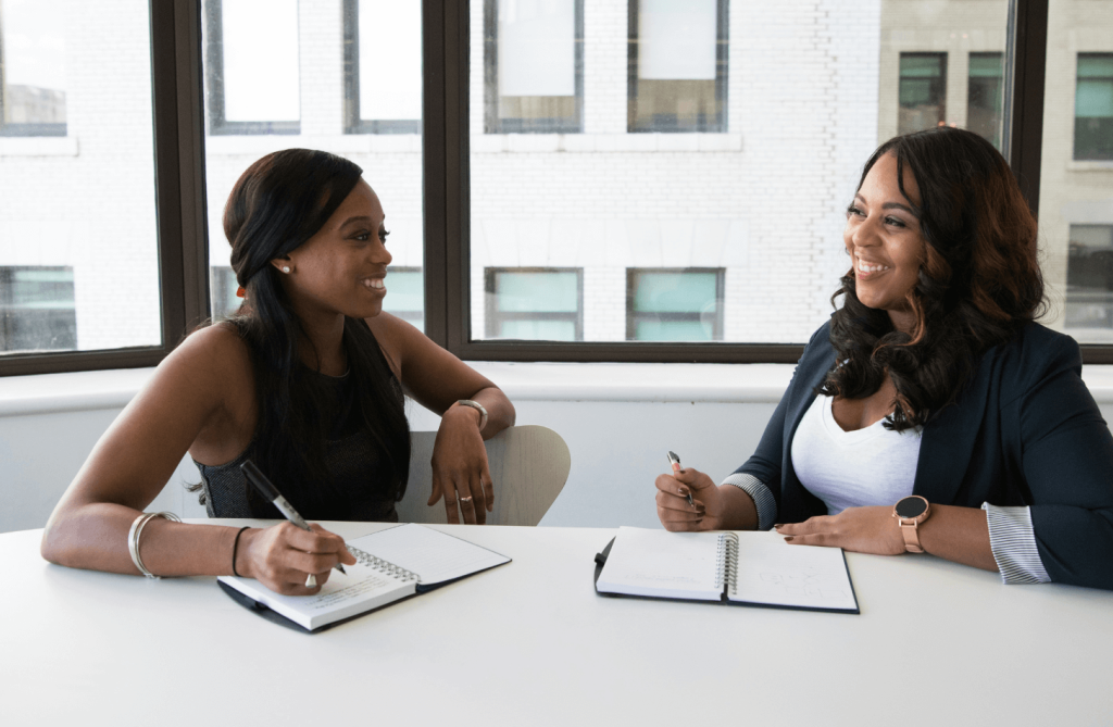 Two women talking, smiling, and taking notes